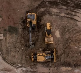 An aerial shot of heavy machinery at a construction site, including excavators and road rollers.