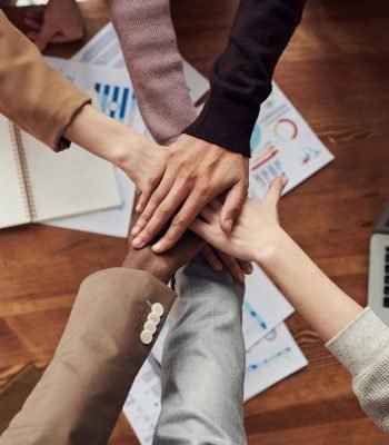 Diverse professionals unite for teamwork around a wooden table with laptops and documents.