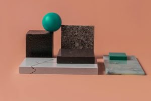 A minimalist geometric arrangement with various textured blocks and a sphere on a peach backdrop.